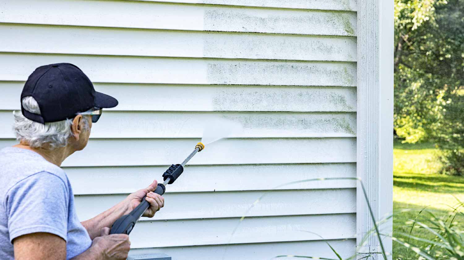 A senior woman pressure washing the siding of a house