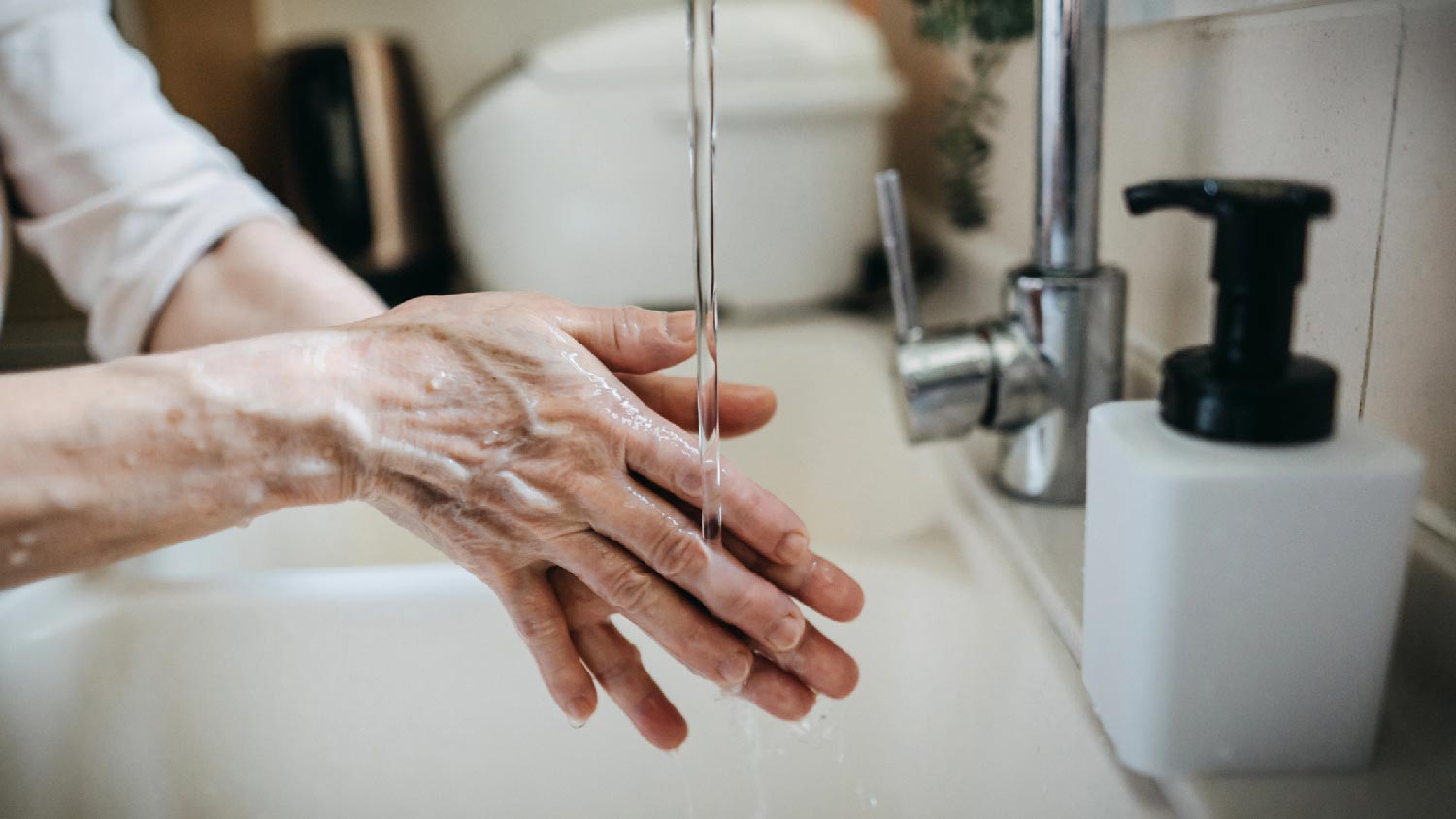 A senior woman washing her hands in the bathroom sink