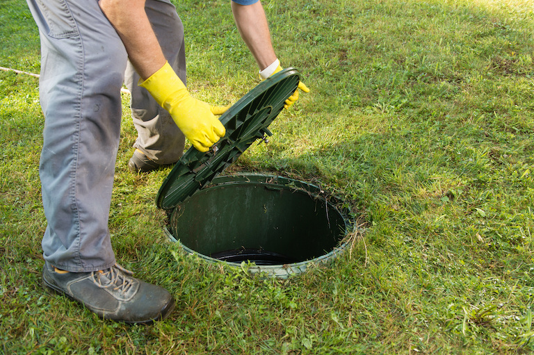 a man lifting a septic tank lid off of the septic tank