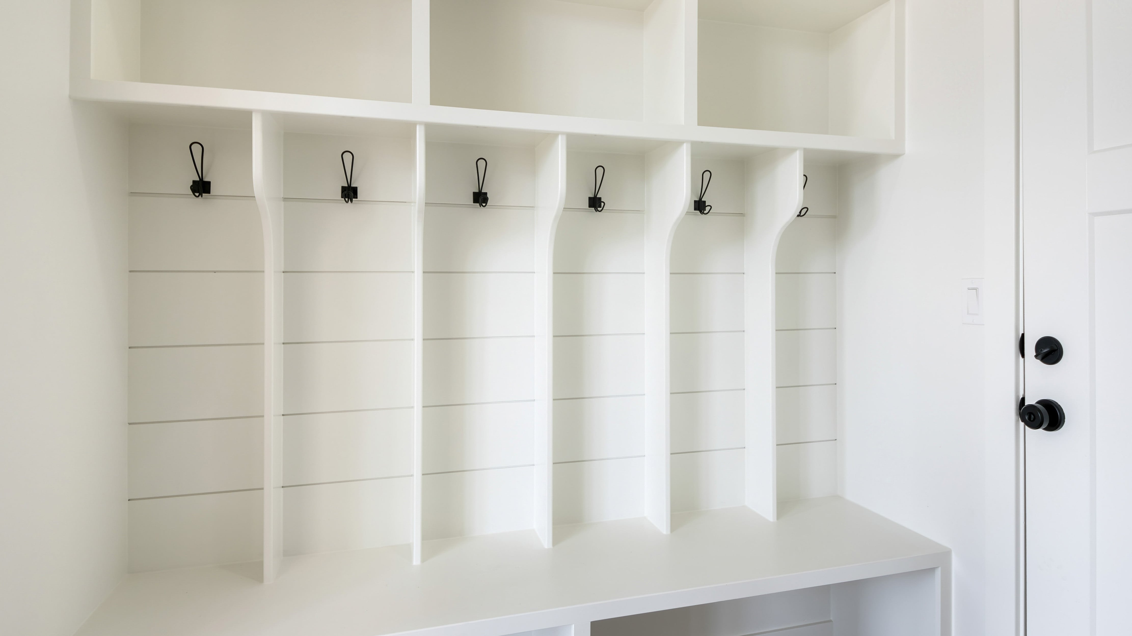 A white mudroom with shiplap accent wall, black hooks, and built-in shelving