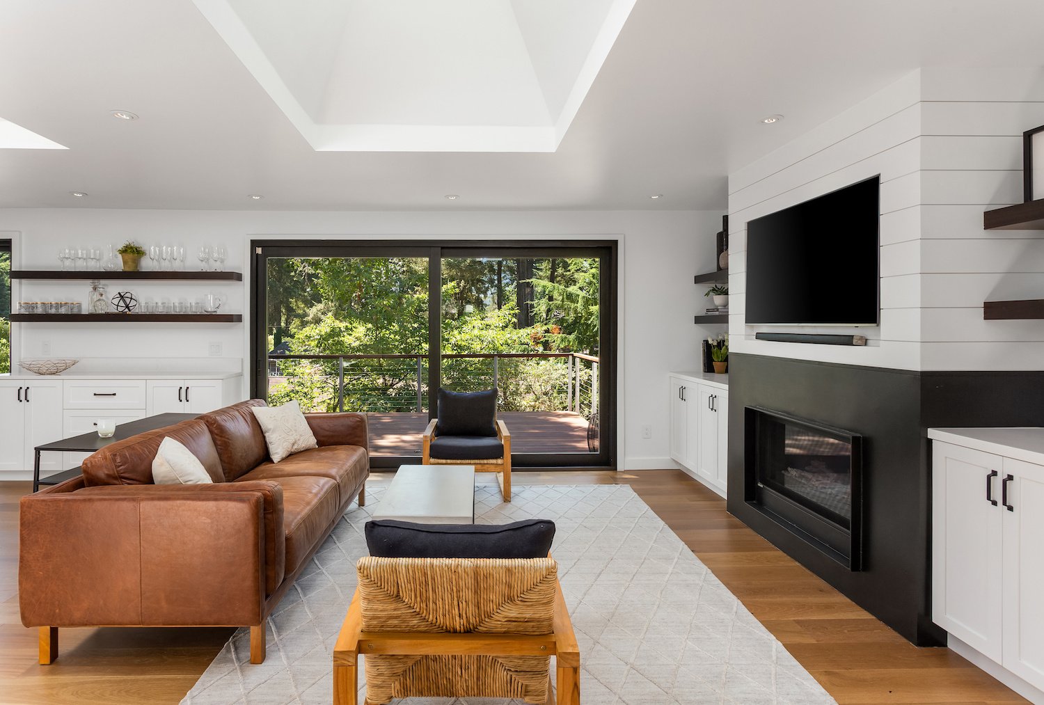 Black and white modern living room with shiplap fireplace and TV wall, skylight, hardwood floors, and patio with glass doors