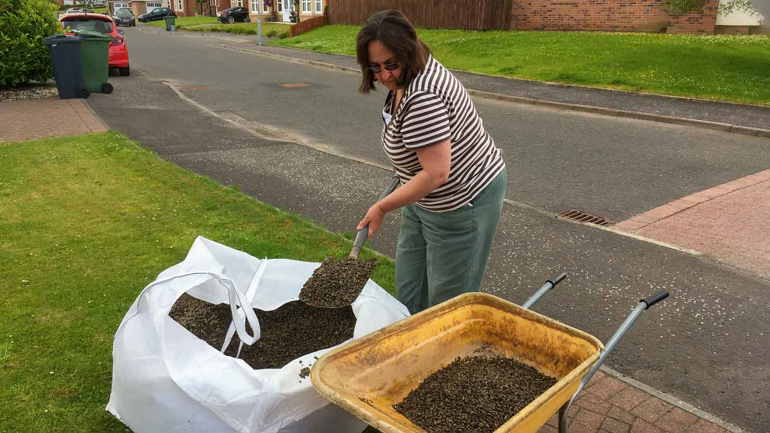 woman shovelling pea gravel into wheel barrow Photo: Tosh/ Adobe Stock