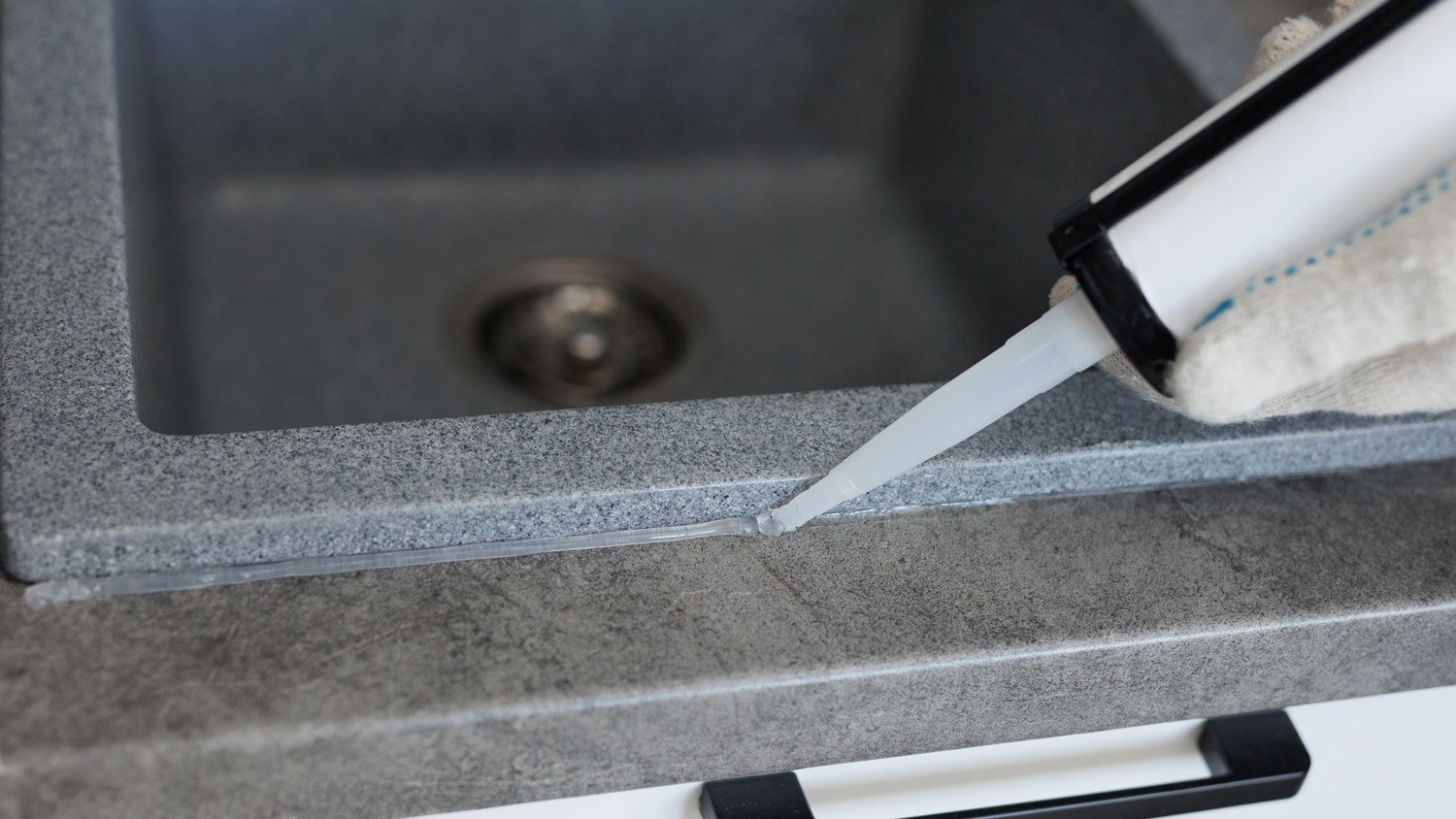 Worker seals up the kitchen sink with a sealant using a construction sealing gun