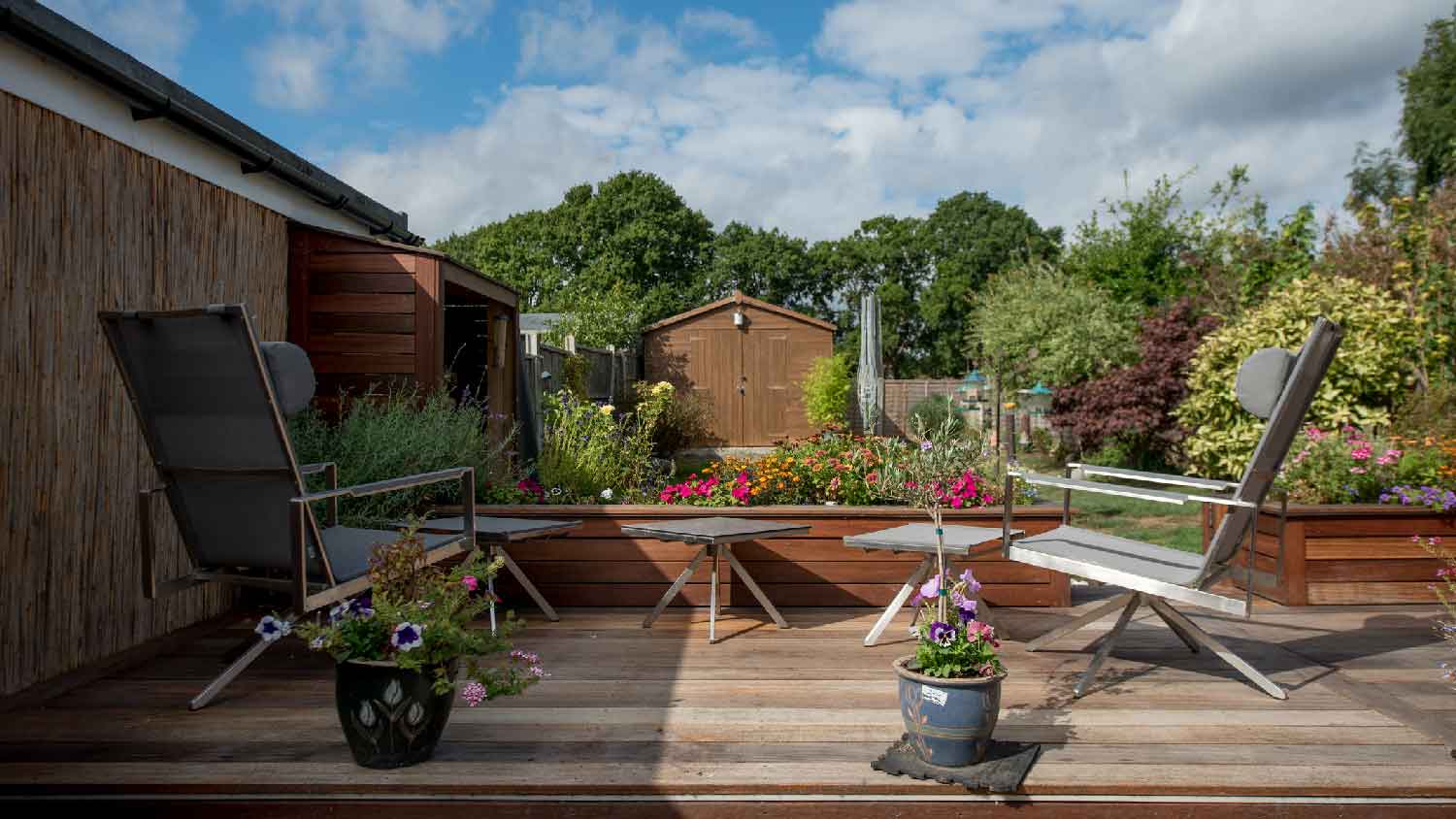 A small wooden deck with garden furniture and flower beds