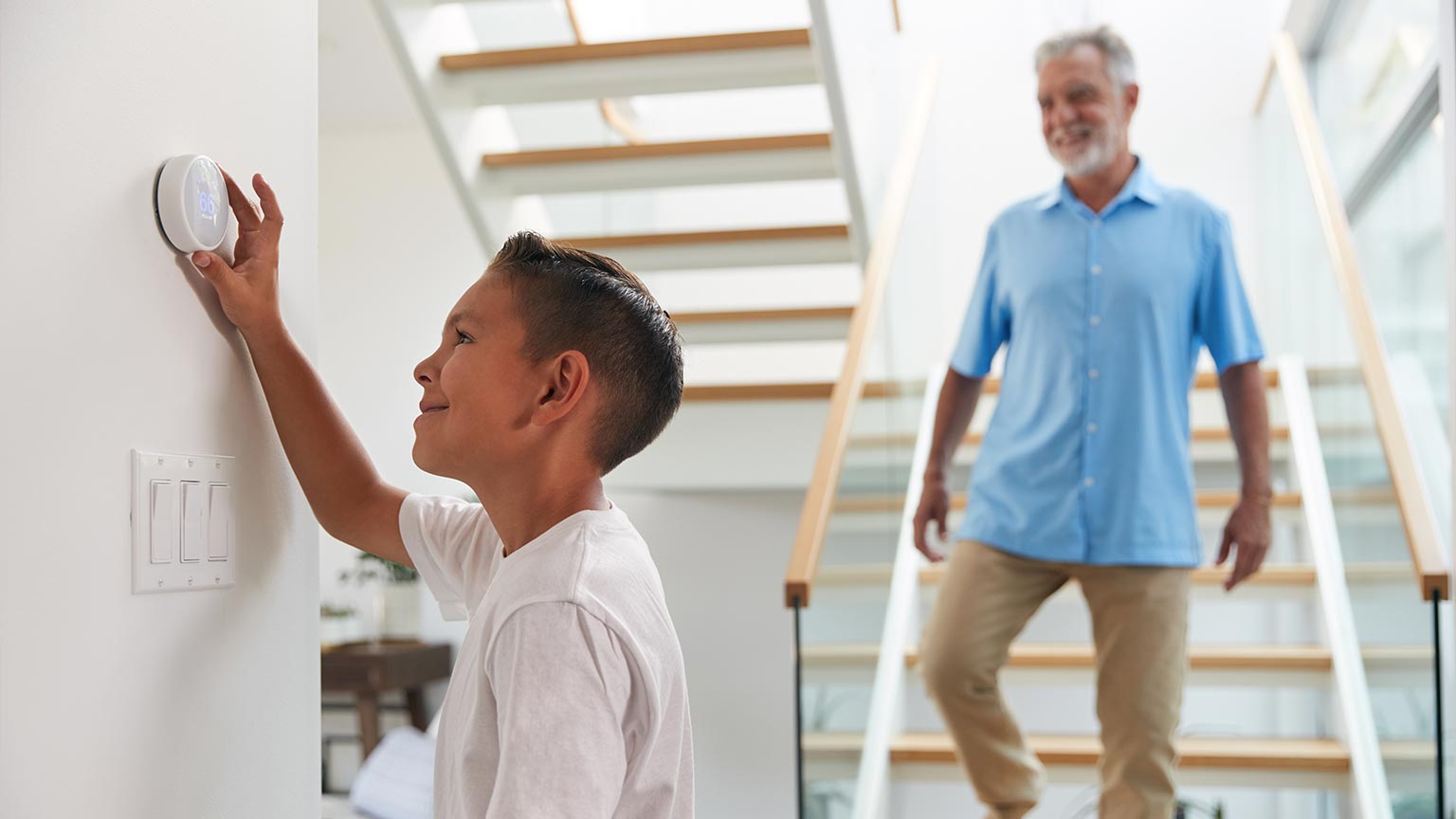 Grandfather With Grandson Adjusting Digital Central Heating Thermostat In Home