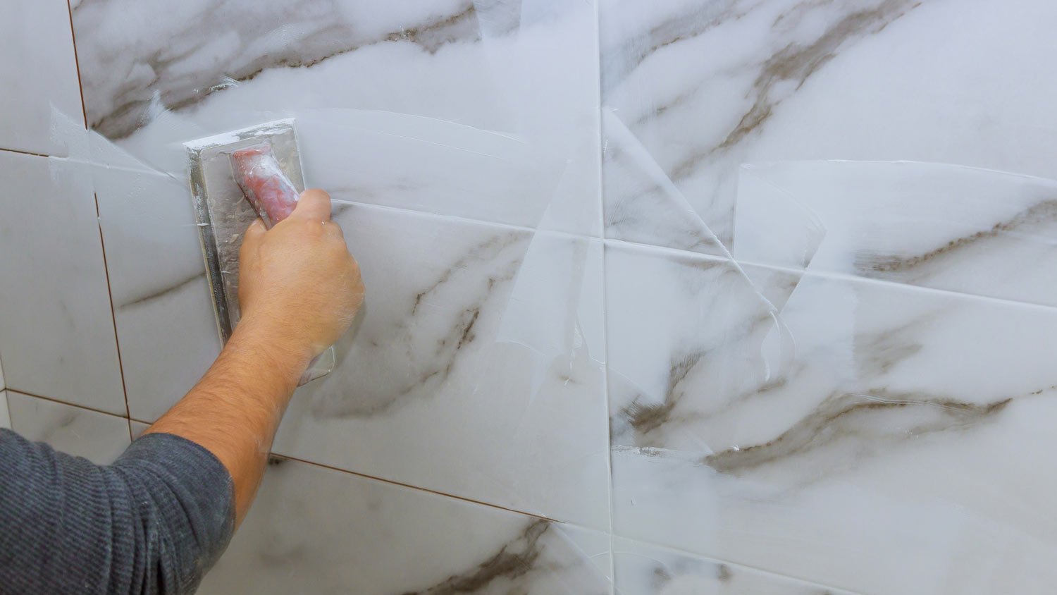 man smoothing out grout on marble tiles