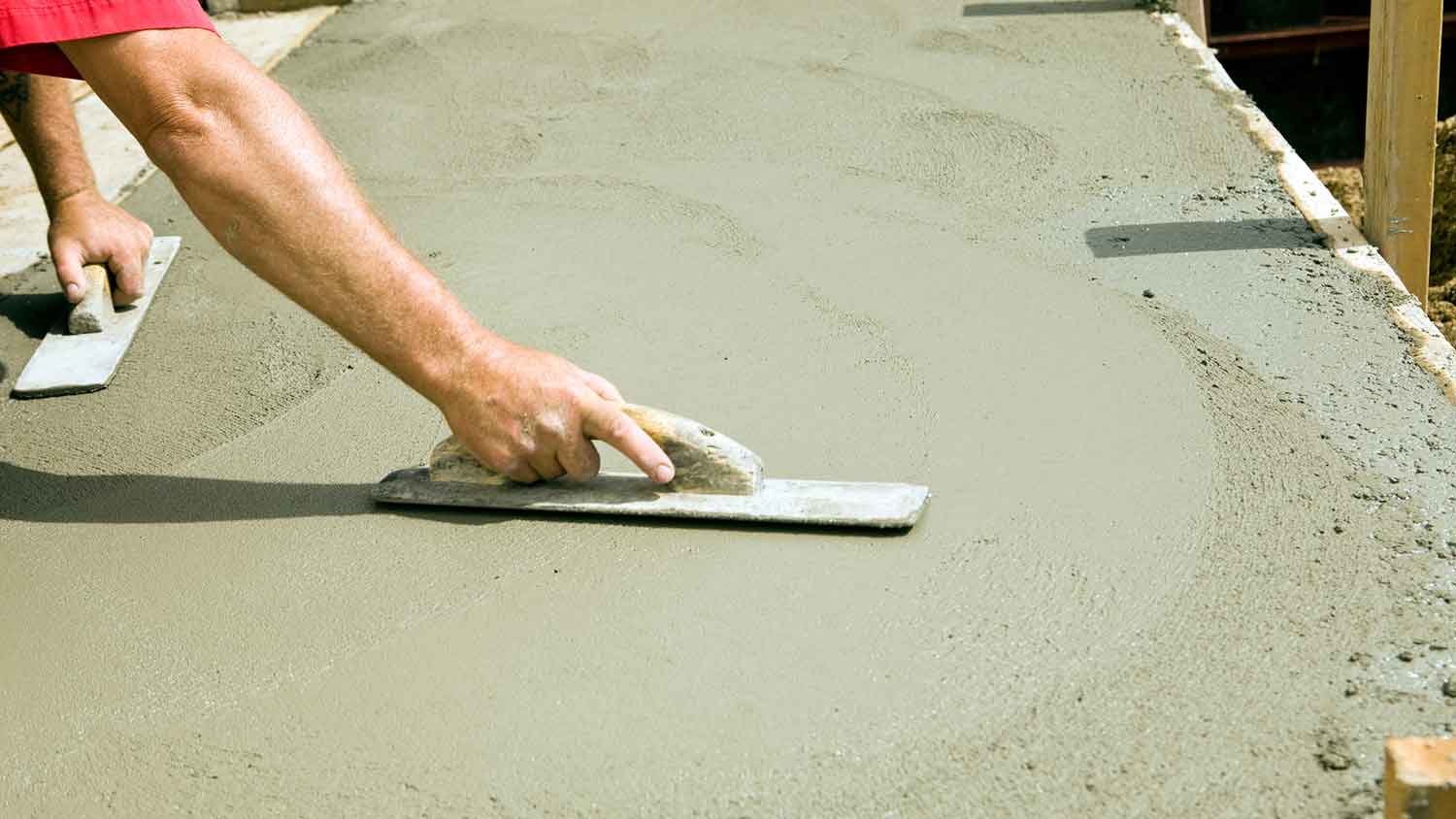 Worker using trowel to smooth fresh concrete