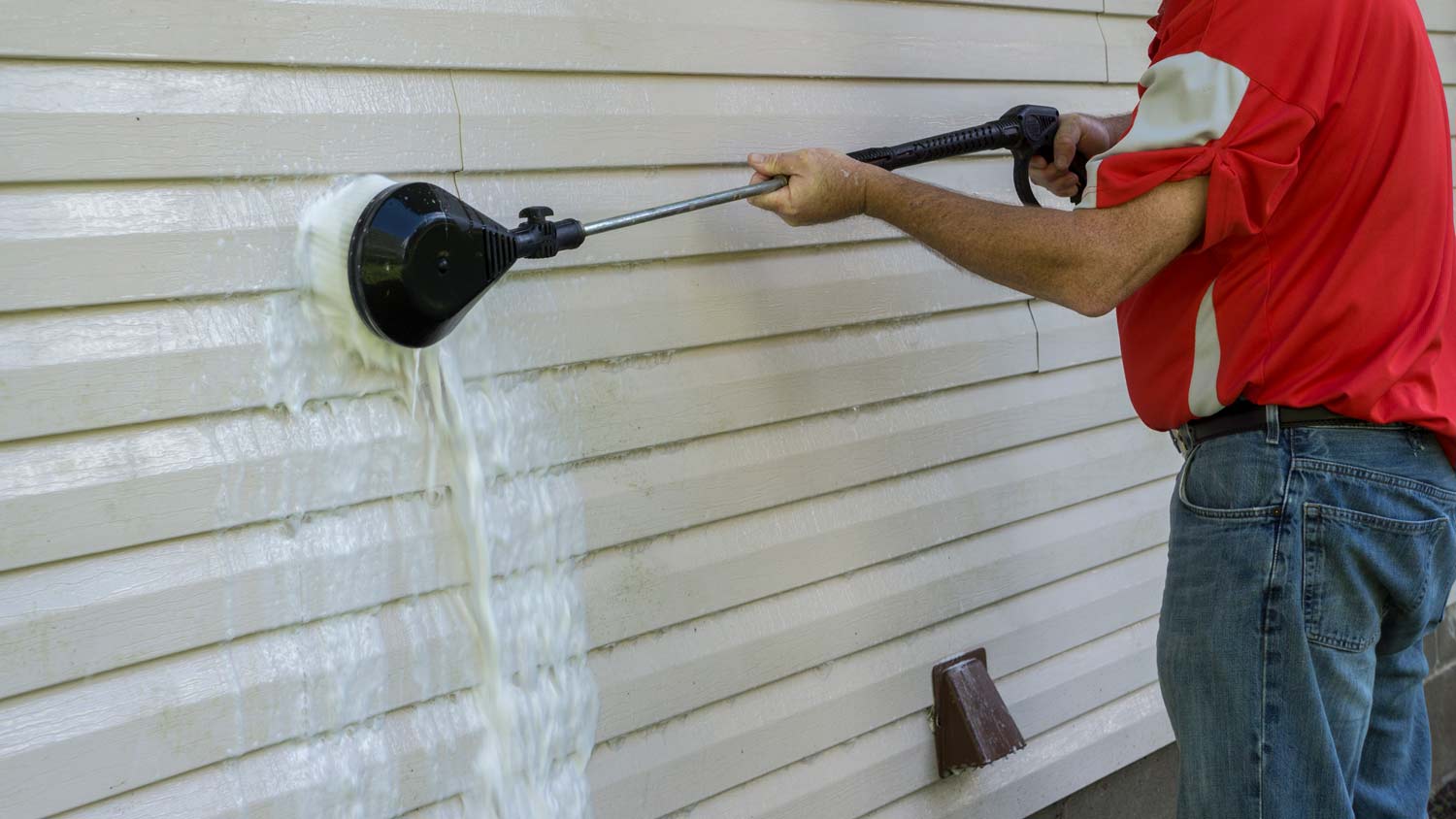 man using soapy pressure brush on vinyl siding