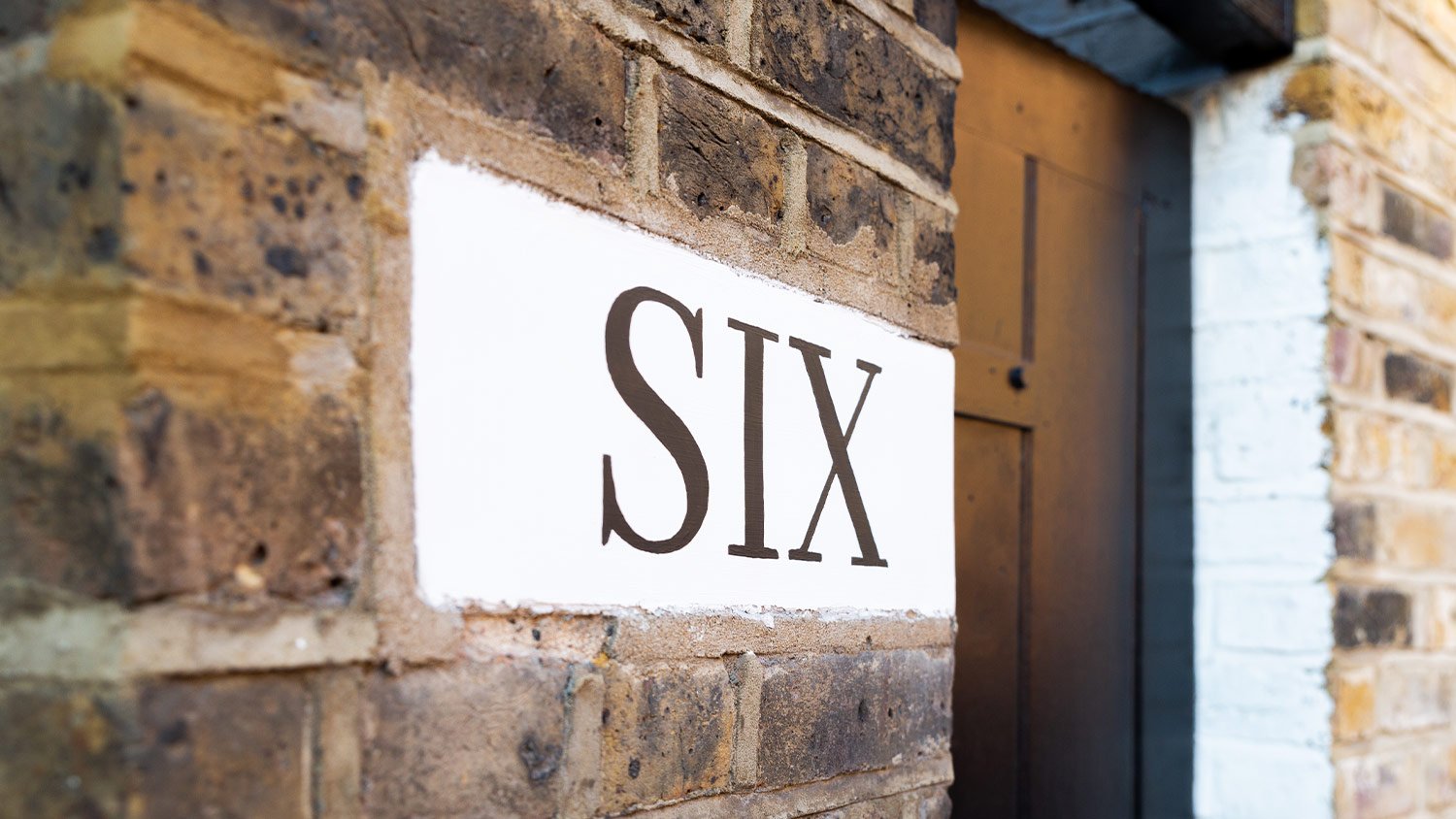 brick home exterior with "Six" on white concrete next to the door 