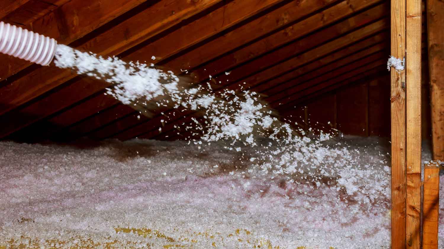 worker spraying blow in insulation in attic