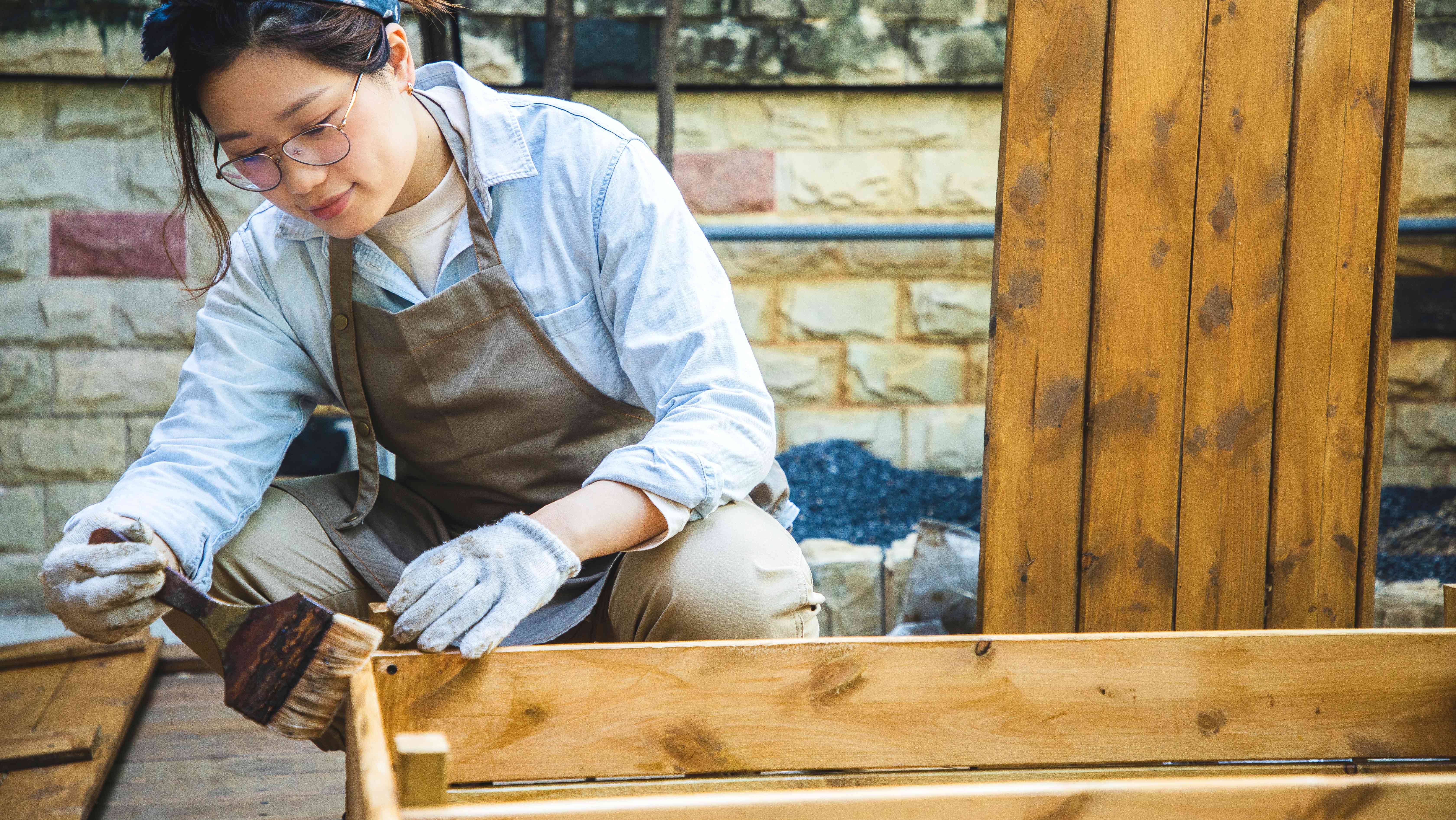 Woman staining wooden bookshelf on the patio 