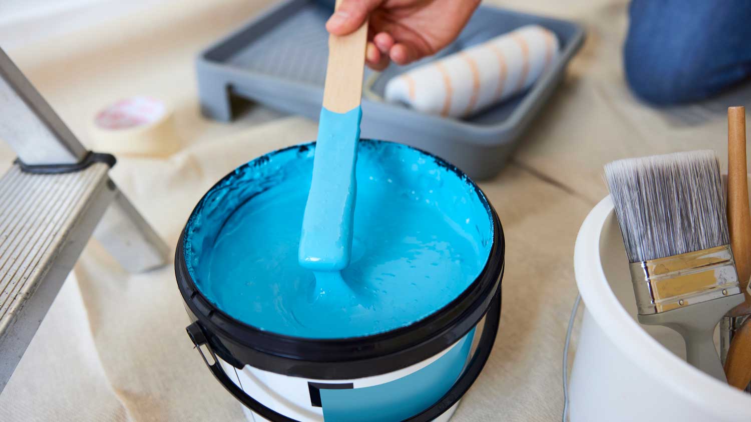 Worker stirring blue paint in a bucket