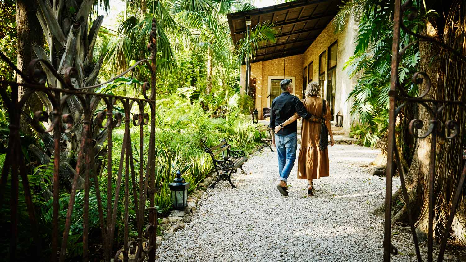 Wide shot rear view of couple walking on path in garden of luxury tropical hotel