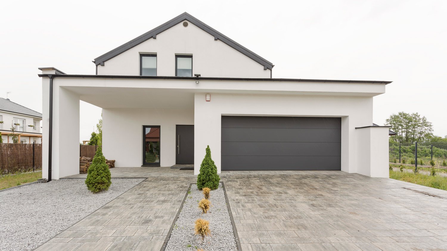 Exterior view of a modern white mansion with a garage and stone driveway