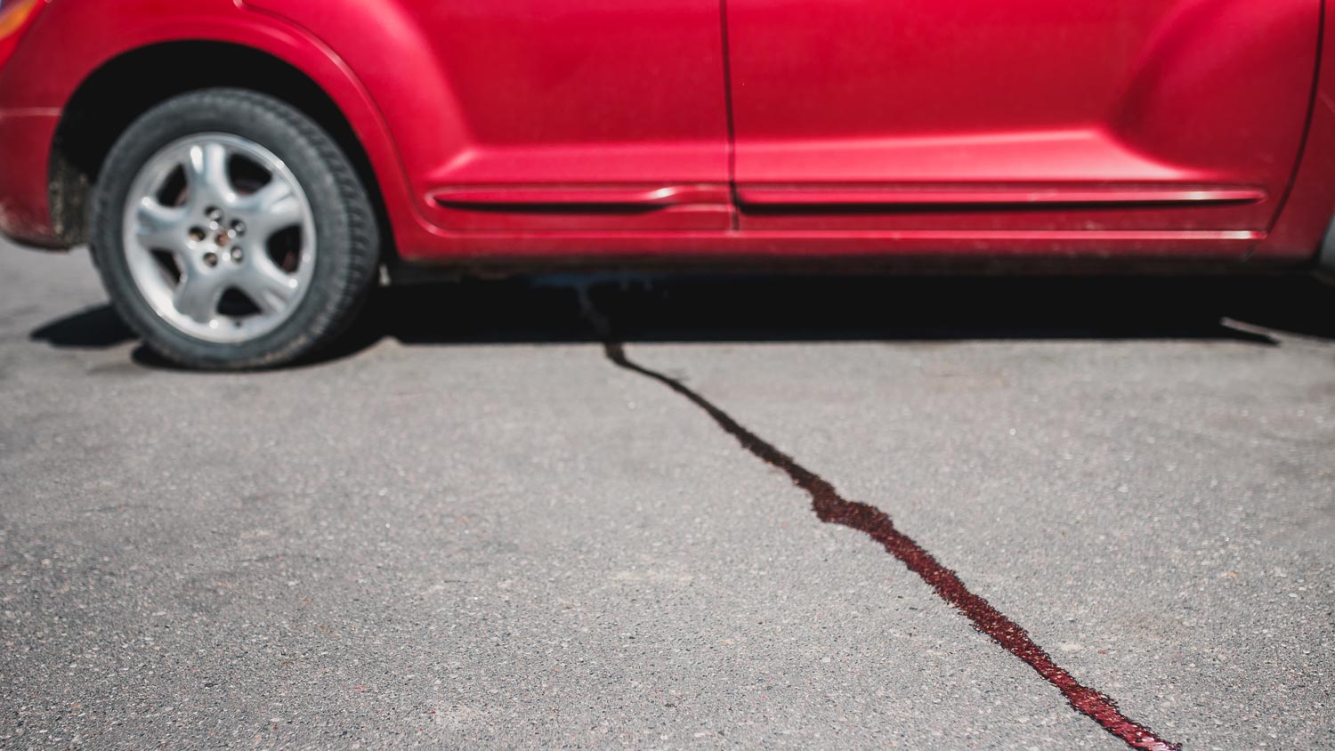 A stream of liquid on a concrete driveway coming under a car