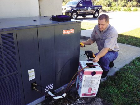 technician performs an outside service check on an air conditioning unit.