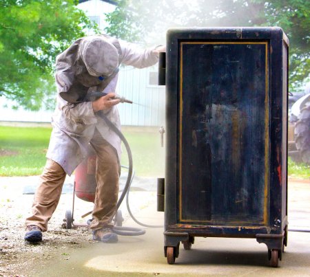 Craftsman using coal slag gun to strip dirt of an antique safe