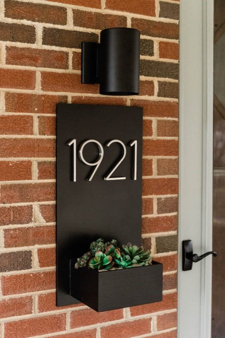 a black planter box displaying the house number and containing a succulent is attached to a brick wall (Photo by © Carrie Waller)