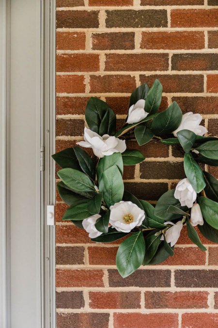 wreath of green leaves and white flowers against red brick wall (Photo by © Carrie Waller)