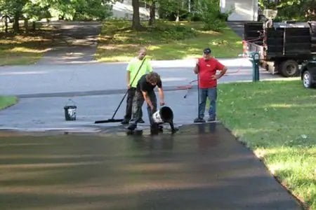 contractor pouring sealant on asphalt driveway