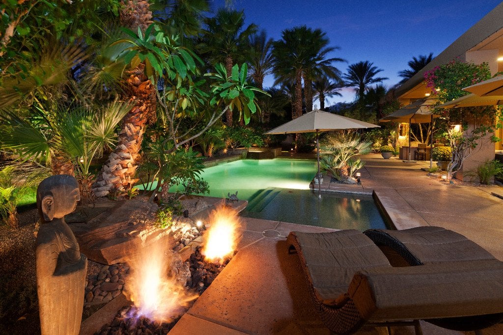 Pool with fire featues, seating, palm trees at night