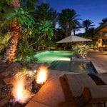 Pool with fire featues, seating, palm trees at night