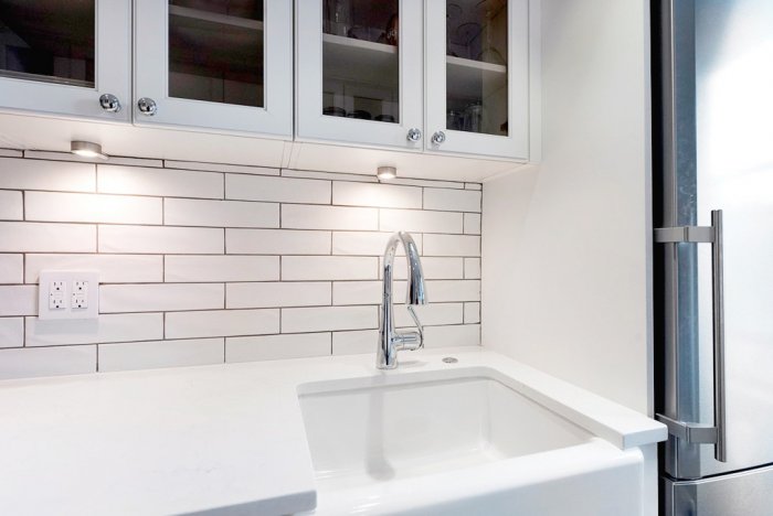 White cabinets and counters with subway tile and apron sink