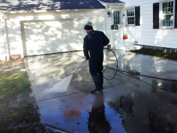 man pressure washing dirty concrete driveway