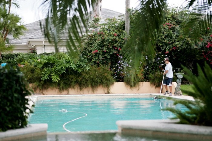 man uses skimmer to clean a swimming pool
