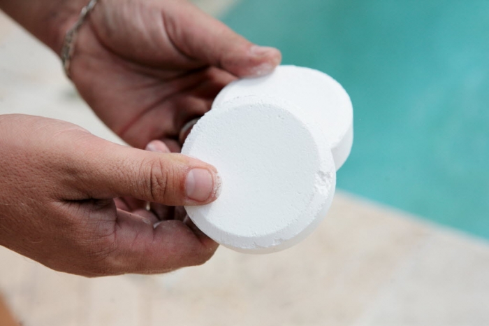 Man holds two large white chlorine capsules near a swimming pool .
