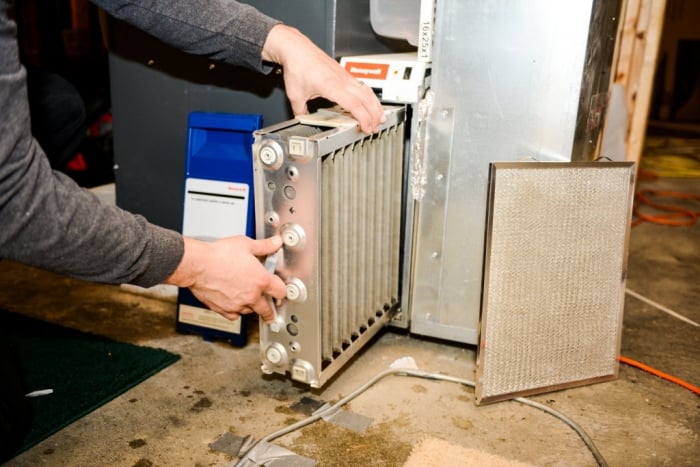 man removes a electronic air cleaner from furnace.