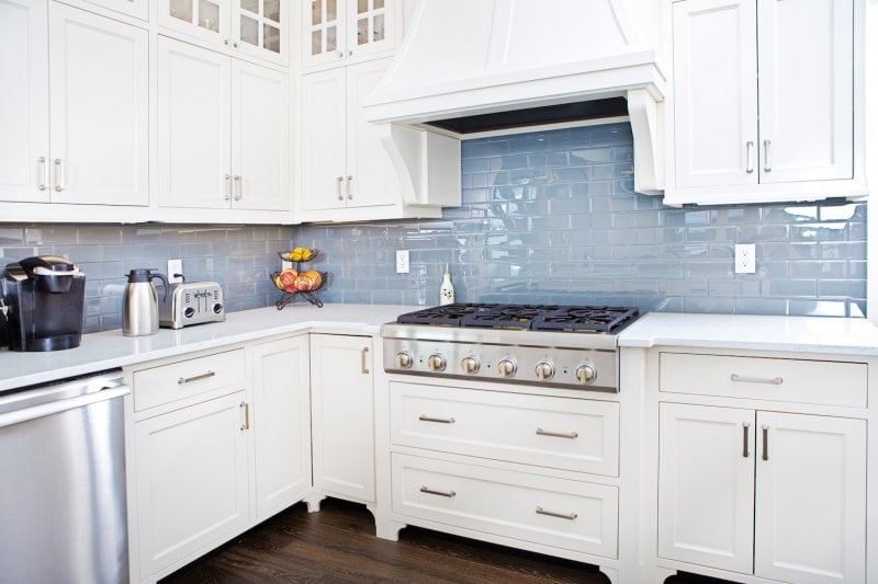 Kitchen with blue-gray iridescent tile backsplash and white cabinets (Photo by YinYang / E+ via Getty Images)