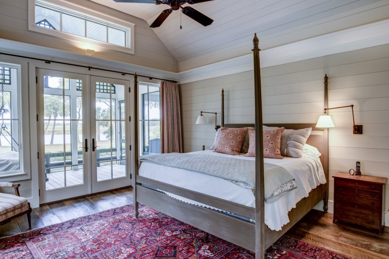 Nautical bedroom with shiplap walls, a wood bed, hardwood floors, and glass patio doors that open onto a porch (Photo by Wollwerth Imagery - stock.adobe.com)
