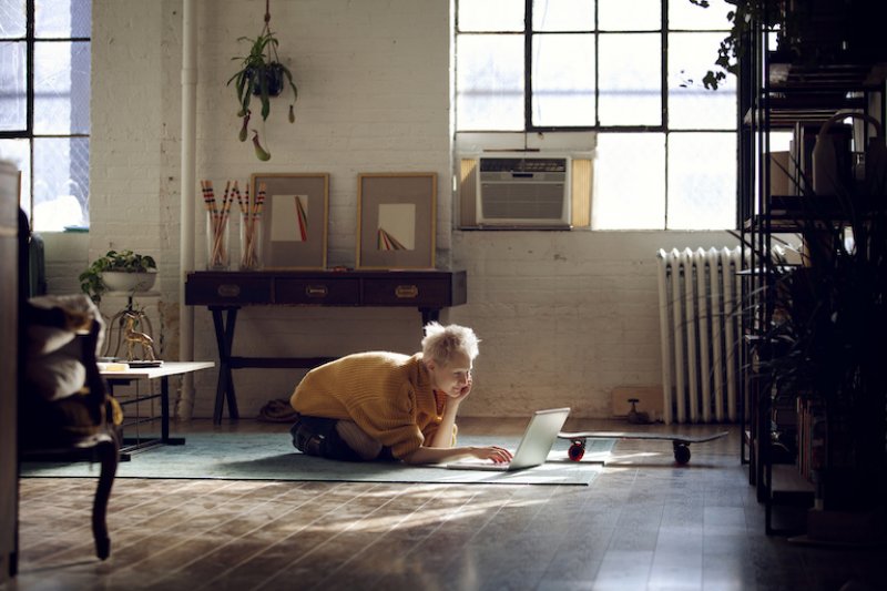 person lays on rug looking at laptop in loft style room with window air conditioner (Photo by Cavan Images/Cavan via Getty Images)