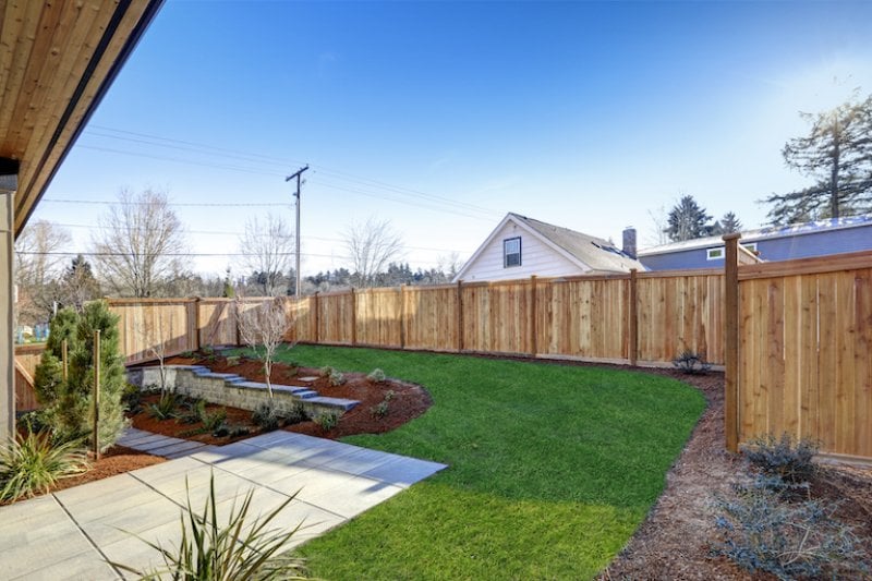 back yard with wood privacy fence, green grass, landscaping with mulch and concrete (Photo by Iriana Shiyan - stock.adobe.com)
