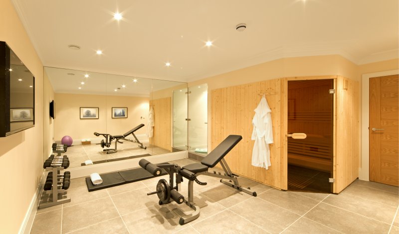 A basement home gym, fitted with exercise equipment including weights, a bench, ball and floor mat. A pine-panelled sauna and shower room are also part of the space. (Photo by phototropic / E+ via Getty Images)