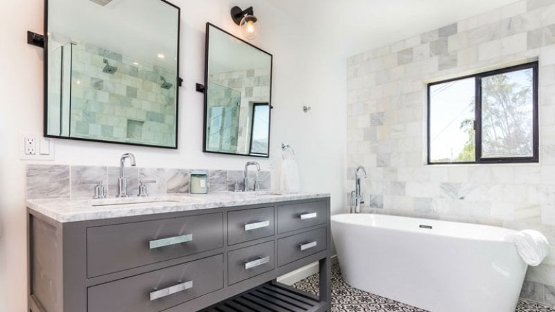 Twin sinks and mirrors in bathroom with white bathtub