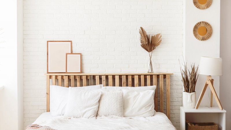 A bed with wooden headboard in an off-white painted bedroom (Photo by Anastasiia Krivenok/Moment via Getty Images)