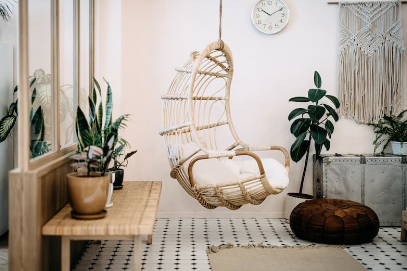 home interior with white, cream, and light wood bohemian decor with hanging chair in middle (Photo by AsiaVision/E+ via Getty Images)