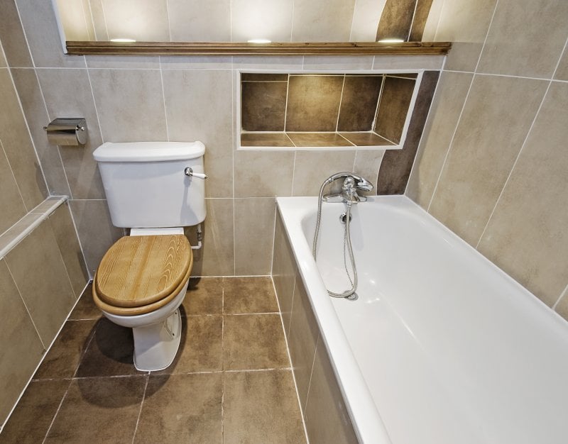 Brown tile bathroom with built-in shower shelves above tub (Photo by yampi – stock.adobe.com)