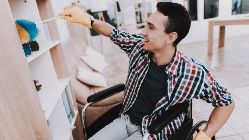 Young man in wheelchair cleaning bookcase (Photo by VGstockstudio / Shutterstock.com)