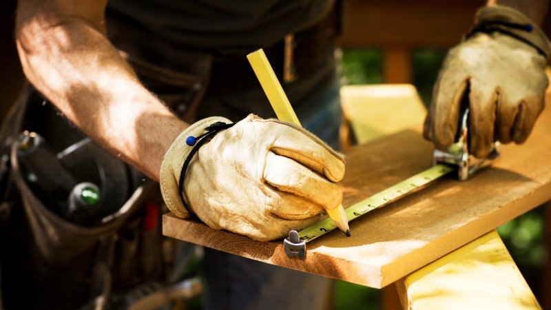 Close-up of a carpenter’s hands in gloves measuring a wooden plank (Photo by stevecoleimages/E+ via Getty Images)