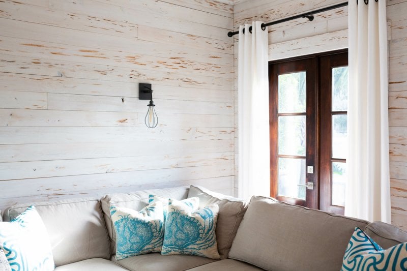 Beach-themed living room with gray couch, nautical throw pillows and white weathered shiplap walls (Photo by KCULP - stock.adobe.com)