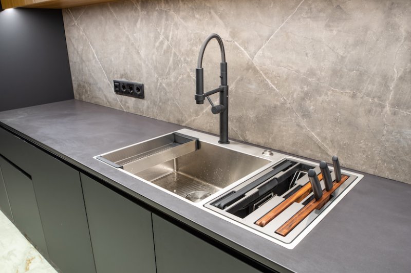 industrial style kitchen with concrete countertop, large stainless steel sink, and dark gray cabinets (Photo by Aleksandr_Kendenko via Getty Images)