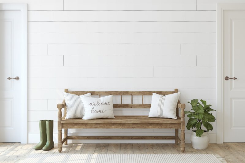 Entryway with boots, a plant and a wooden bench with throw pillows in front of a white shiplap accent wall between two doors (Photo by poligonchik - stock.adobe.com)