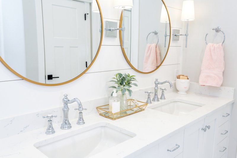 White bathroom vanity in front of white shiplap bathroom accent wall with two gold circle mirrors (Photo by LUGOSTOCK - stock.adobe.com)