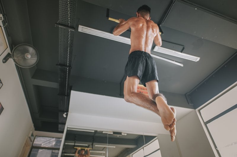 Man doing pull ups in his garage home gym facing a mirror with a fan in the upper left hand corner (Photo by Edwin Tan / E+ via Getty Images)