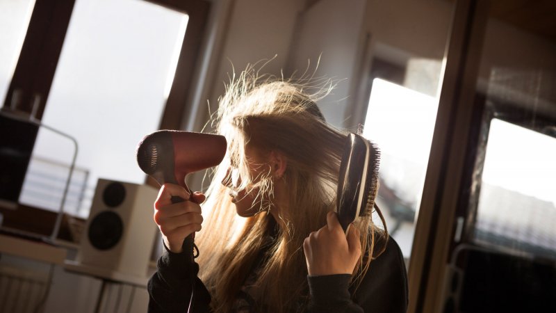 A girl blow drying her hair (Photo by Elva Etienne/Moment via Getty Images)