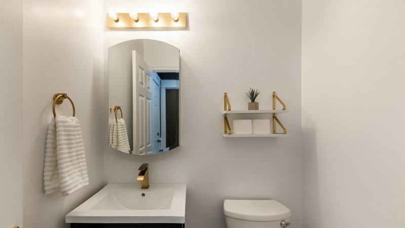 Small powder room with matching gold faucet, towel ring, and open-concept shelf (Photo by Jason – stock.adobe.com)