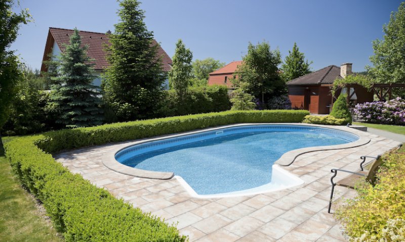 home swimming pool with stone patio and shrubbery and houses in background (Photo by kropic - stock.adobe.com)